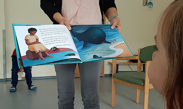 Die Erzieherin zeigt zwei Seiten des Buches mit Jona und mit dem Wal.