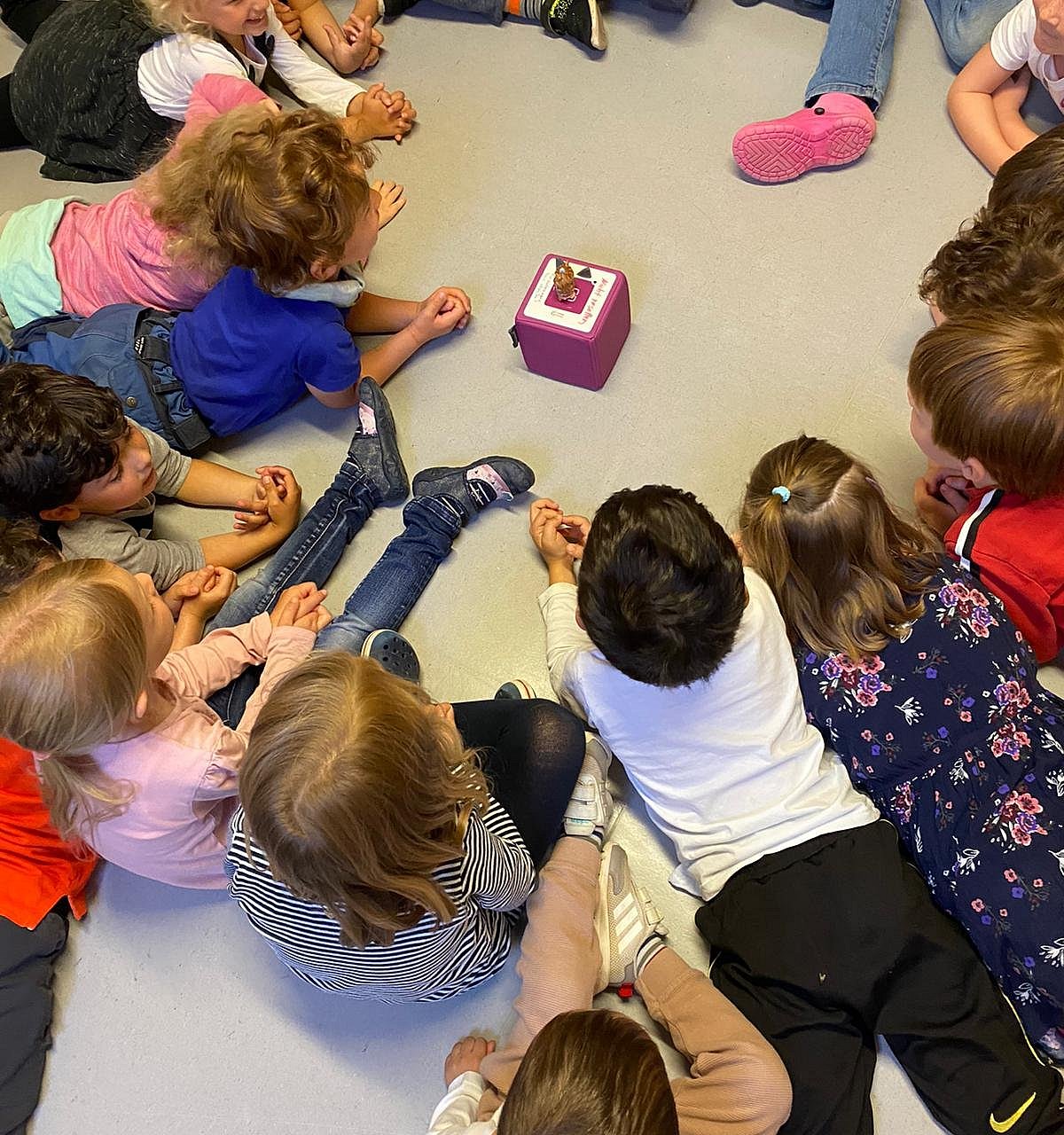 Die Kinder liegen im Kreis um die Tonie-Box und hören eine Geschichte